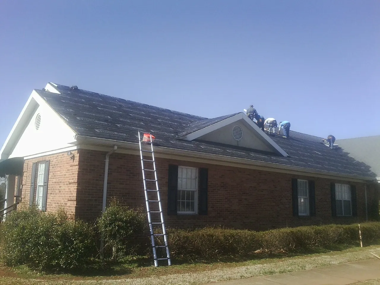 Crew tearing shingles off a brick ranch roof with a ladder set — Emergency Roof Repair work by our crew in Seneca