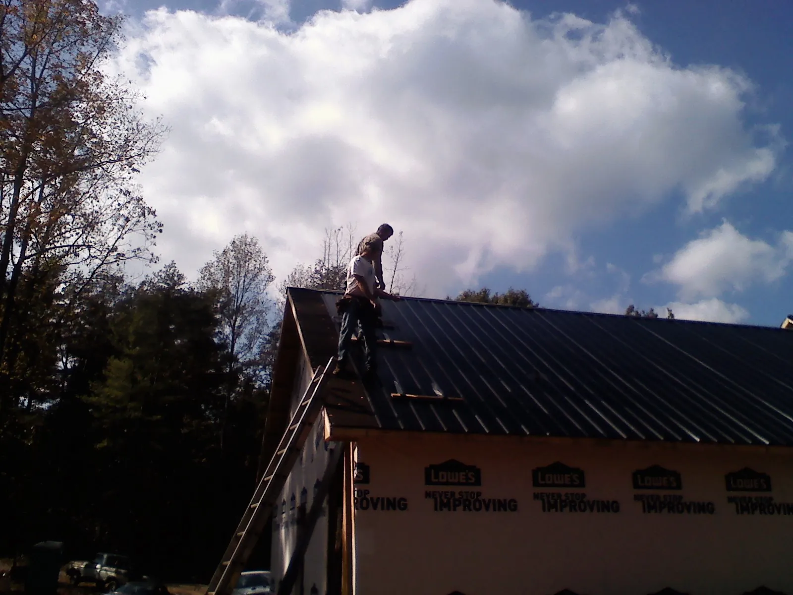 Roofer fastening dark metal panels high against a cloudy sky, from a Roof Inspection job in Seneca