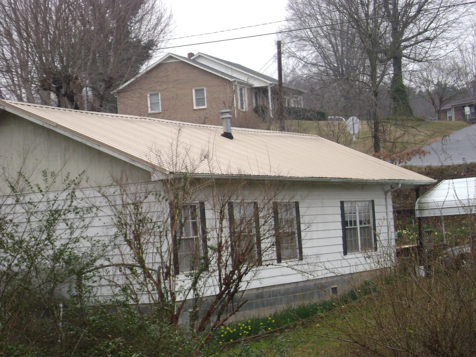 Tan metal roof on a white sided house set into a hillside — Commercial Roofing by Roofing Brothers in Seneca
