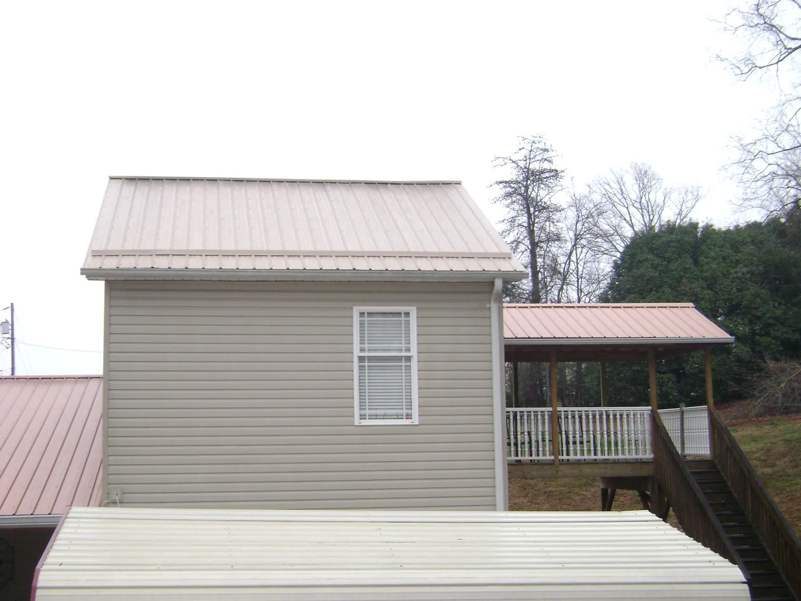 Tan metal roofs on a two story addition and attached porch, from a Roof Replacement job in Seneca